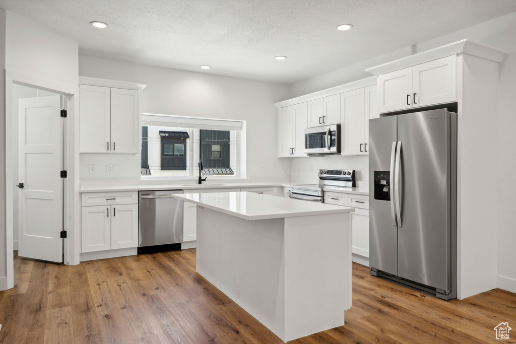 Kitchen featuring stainless steel appliances, white cabinets, light countertops, a center island, and recessed lighting