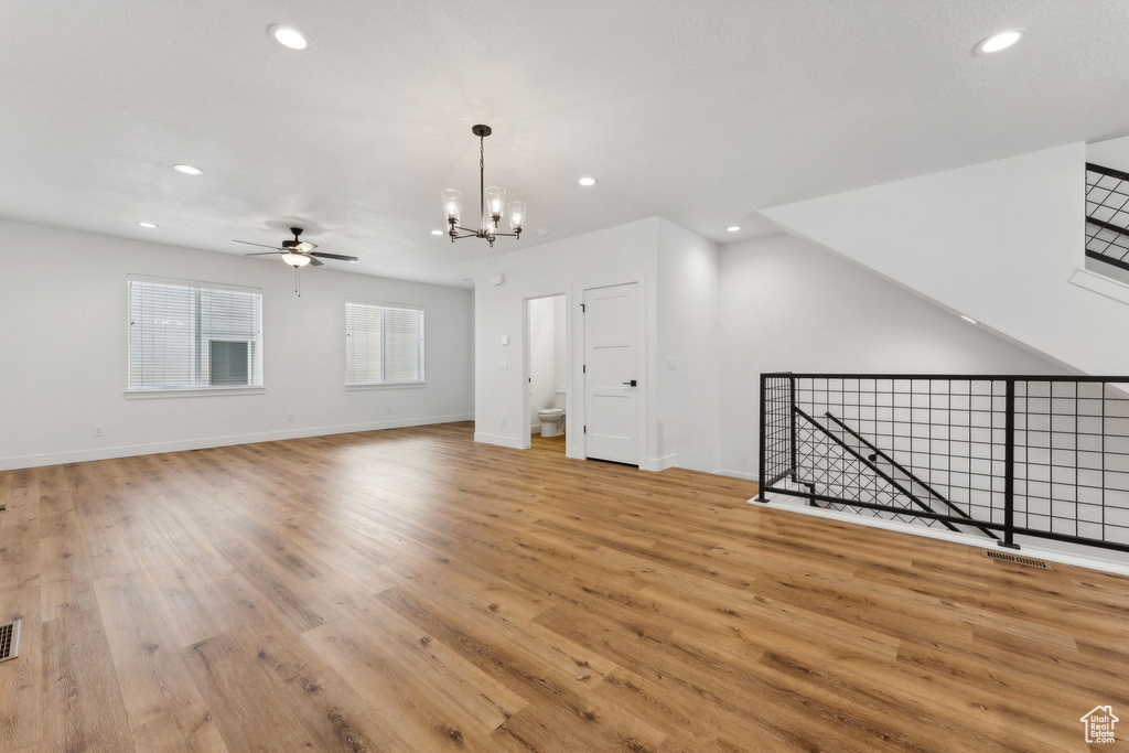 Unfurnished living room featuring a ceiling fan, a chandelier, recessed lighting, light wood finished floors, and baseboards