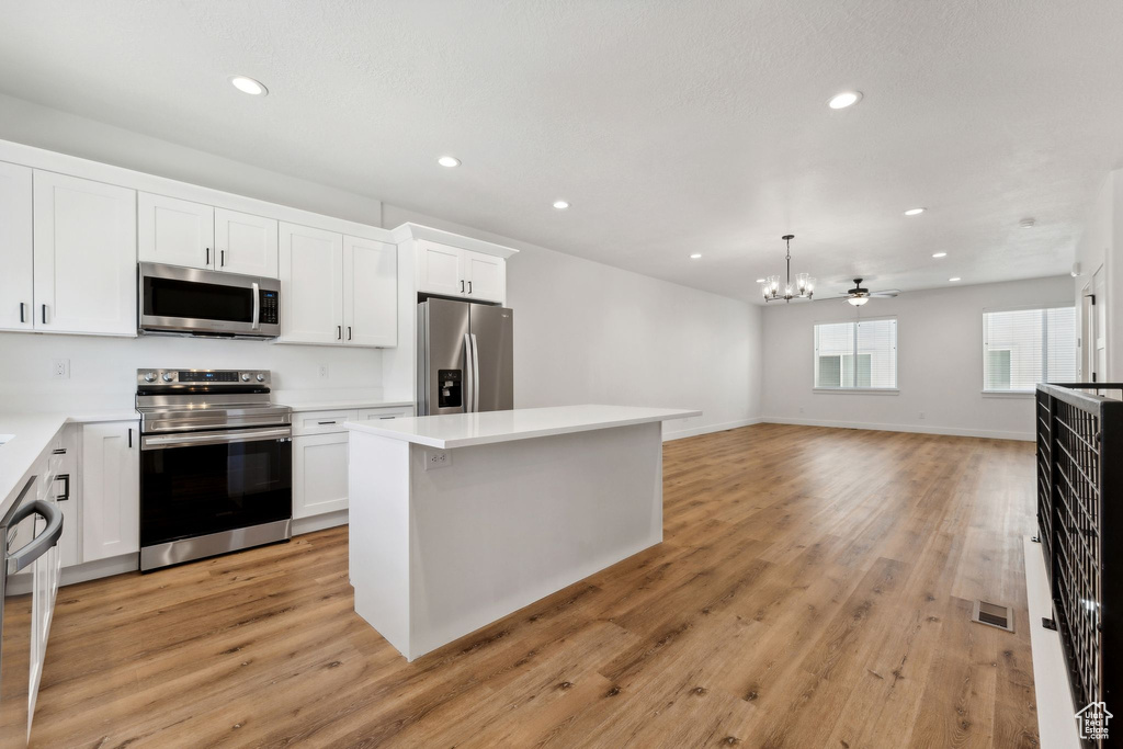 Kitchen with appliances with stainless steel finishes, a chandelier, recessed lighting, white cabinetry, and a center island