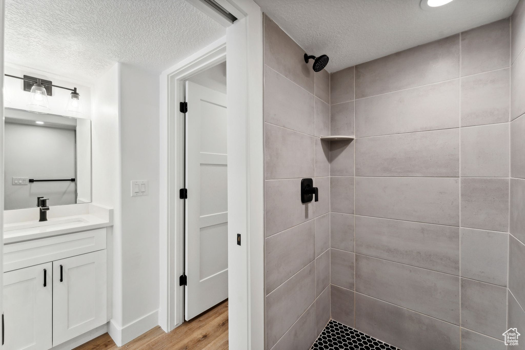 Bathroom featuring a textured ceiling, tiled shower, vanity, and wood finished floors