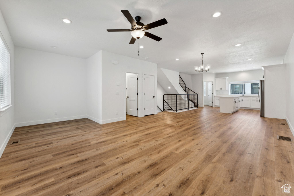 Unfurnished living room featuring recessed lighting, a chandelier, a ceiling fan, light wood-type flooring, and stairs