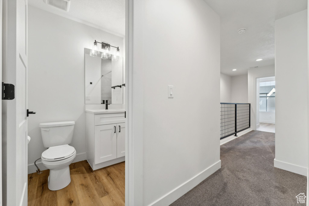Bathroom with vanity, toilet, baseboards, wood finished floors, and recessed lighting
