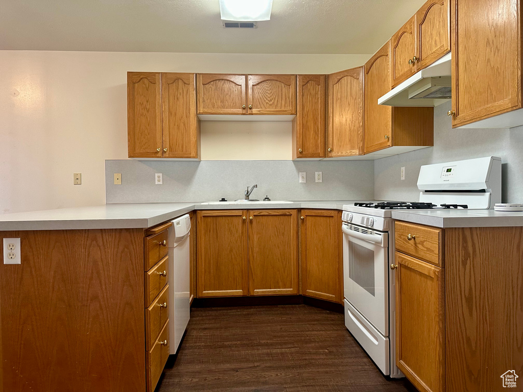 Kitchen with white appliances, under cabinet range hood, dark wood-style floors, and light countertops
