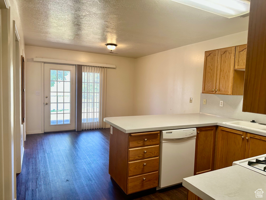 Kitchen featuring dishwasher, a peninsula, dark wood finished floors, light countertops, and a textured ceiling