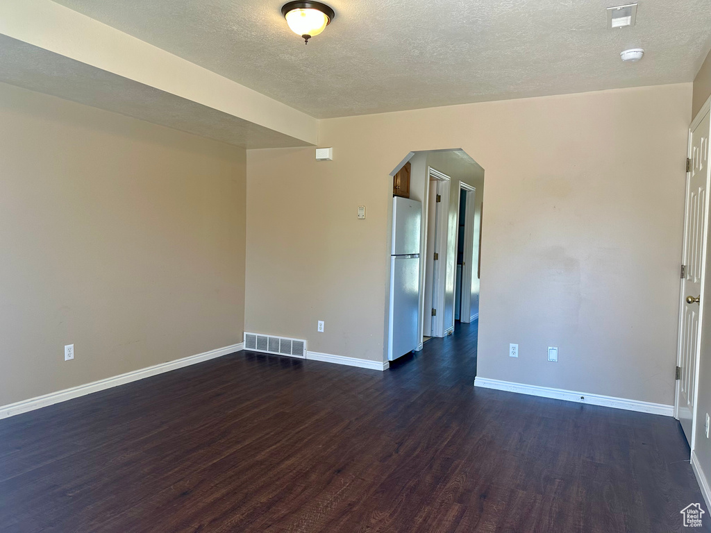 Spare room with arched walkways, dark wood finished floors, a textured ceiling, and a smoke detector