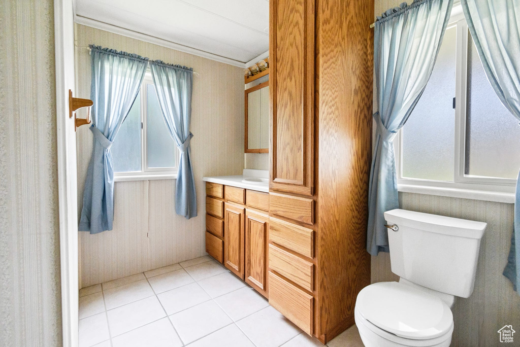 Half bathroom featuring healthy amount of natural light, vanity, toilet, tile patterned floors, and wallpapered walls