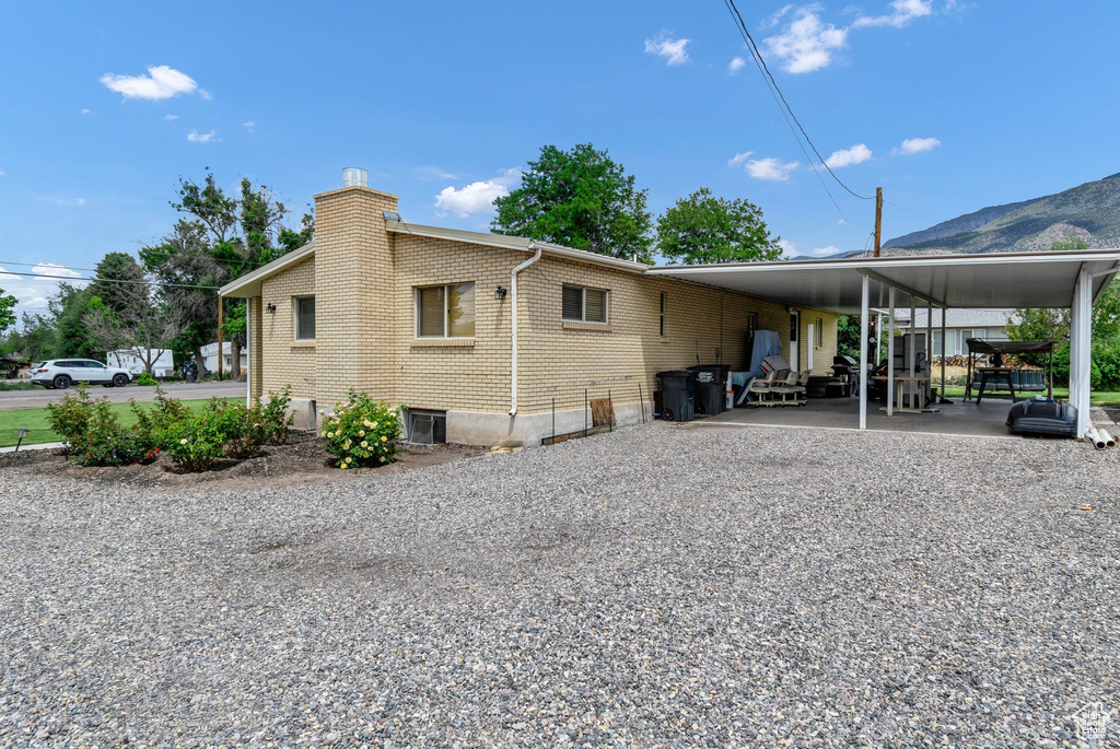 Back of property with a chimney, an attached carport, brick siding, driveway, and a mountain view