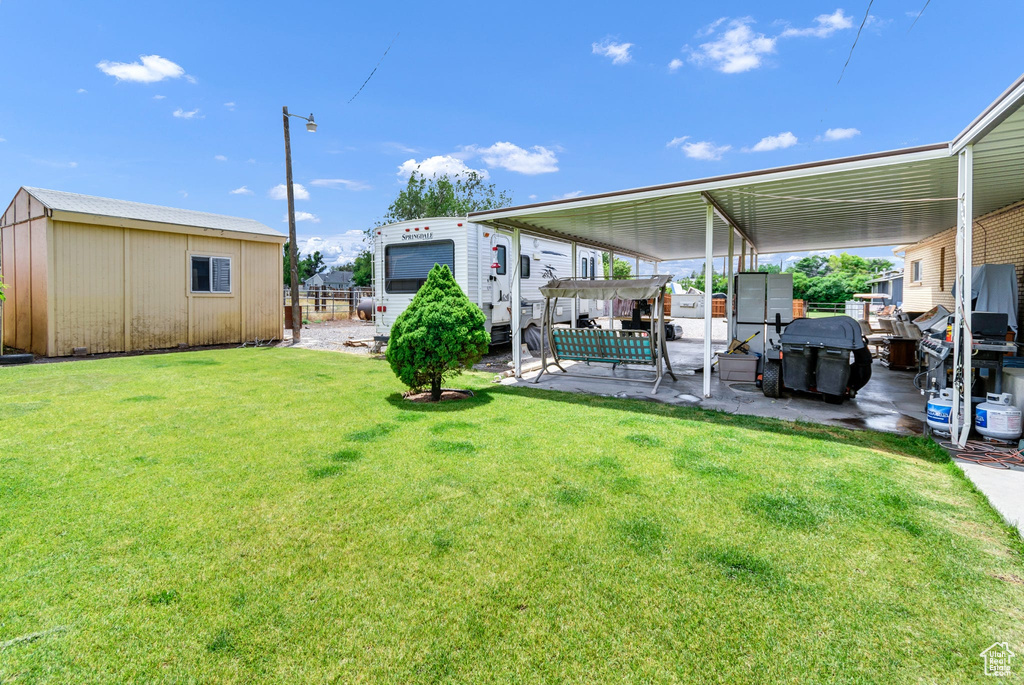 View of green lawn featuring a patio area, an outdoor structure, a pergola, and a carport