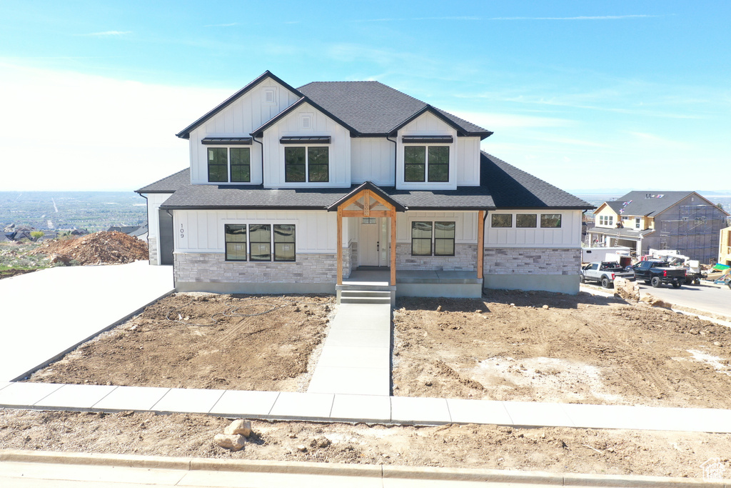 Modern farmhouse featuring stone siding, roof with shingles, and a porch