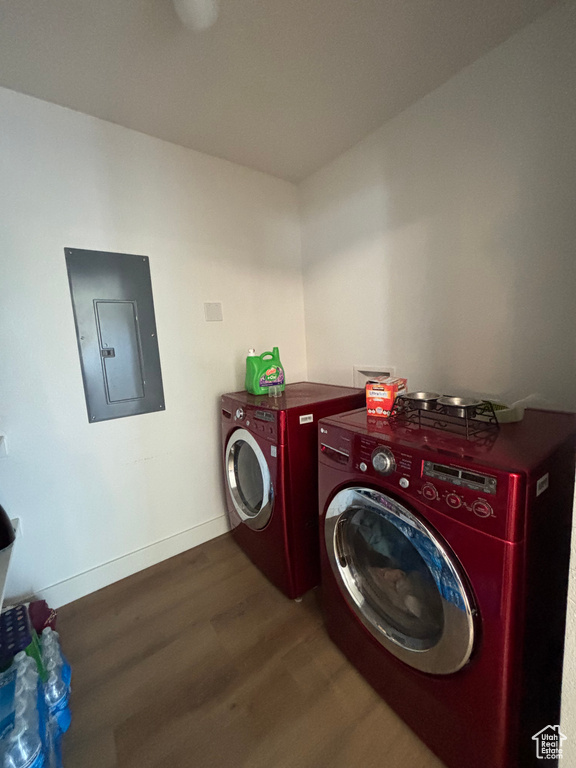 Laundry room with electric panel, washing machine and dryer, wood finished floors, and baseboards