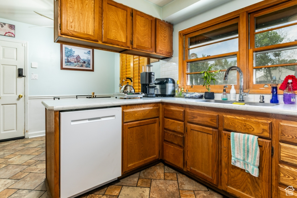 Kitchen featuring dishwasher, stone tile floors, light countertops, and brown cabinetry