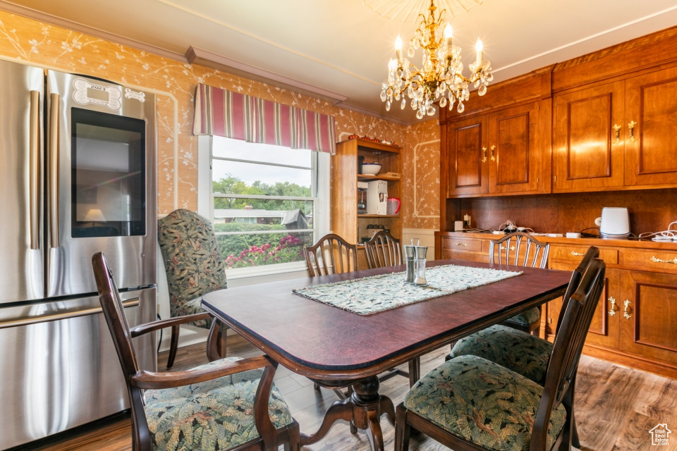 Dining room featuring wallpapered walls, a chandelier, wood finished floors, and ornamental molding