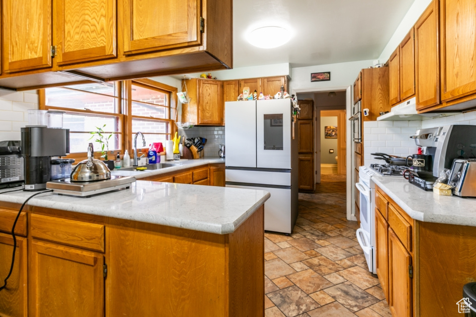 Kitchen with white appliances, brown cabinetry, tasteful backsplash, stone finish flooring, and a peninsula