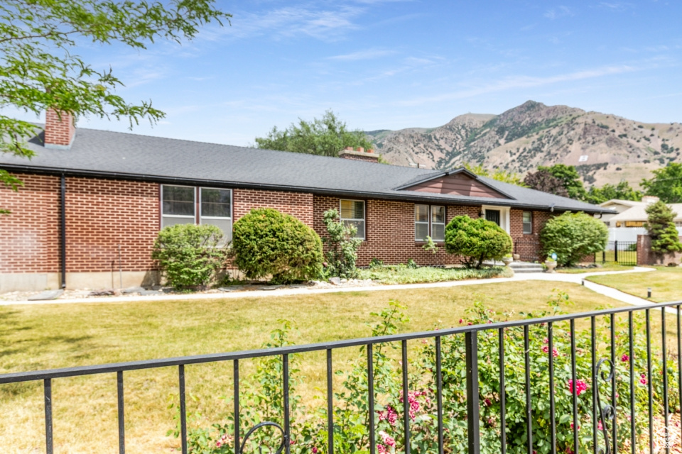 Ranch-style home with a chimney, brick siding, a mountain view, and a front yard
