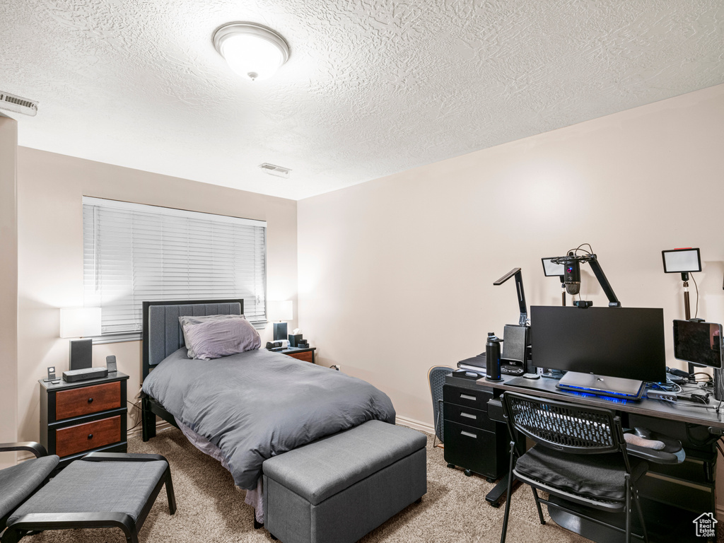 Bedroom with light carpet, a textured ceiling, a desk, and baseboards