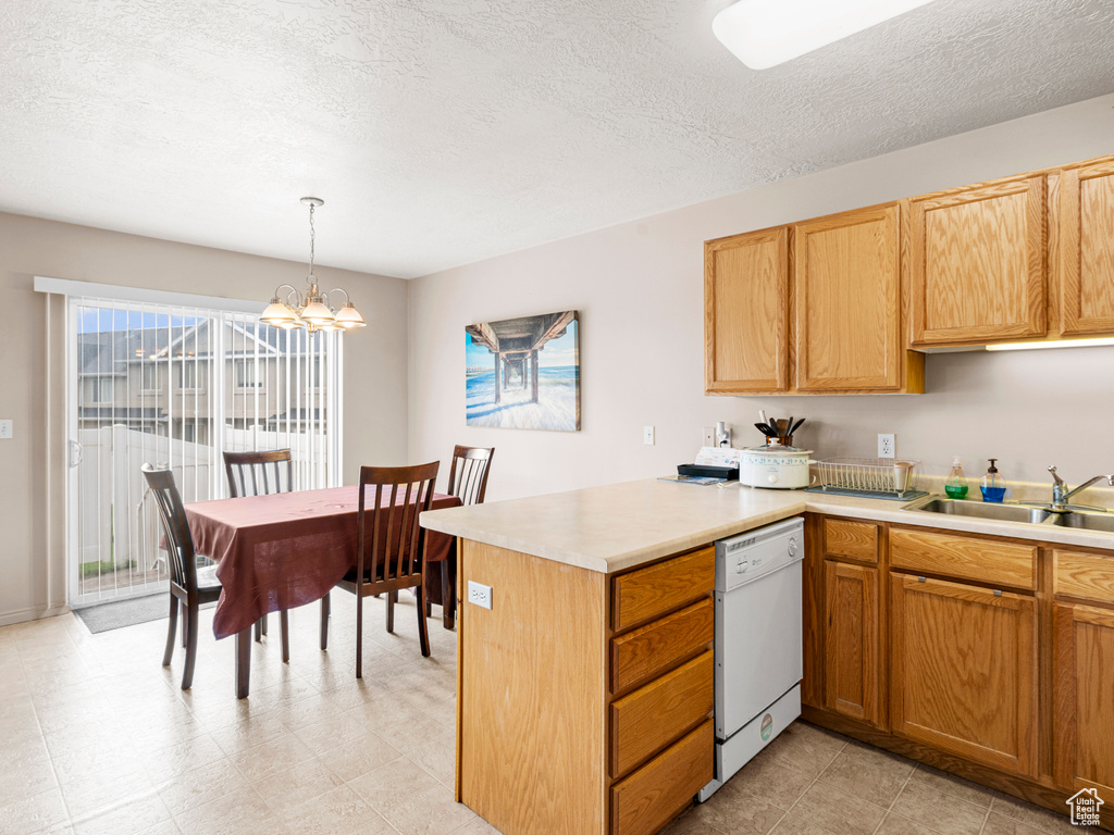 Kitchen with white dishwasher, a sink, a peninsula, light countertops, and a chandelier