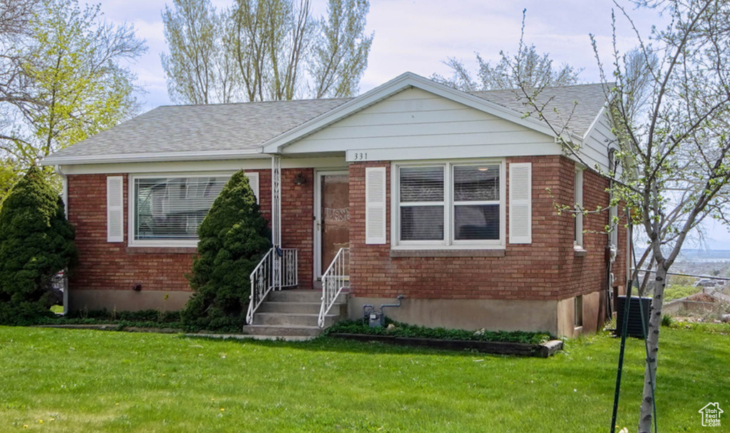 Bungalow featuring a front yard, brick siding, and central AC