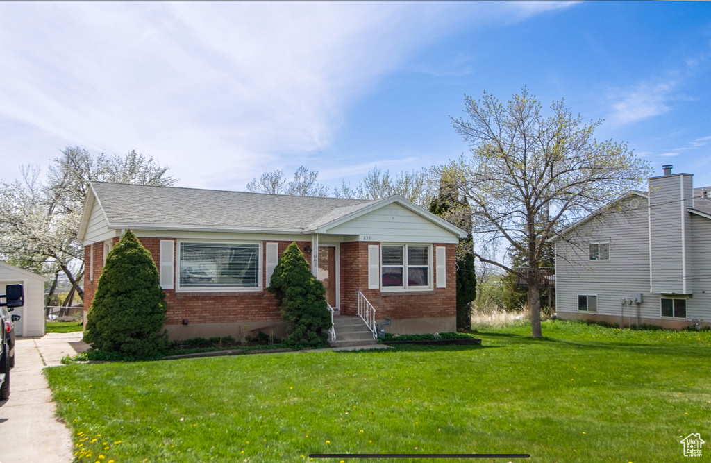 View of front of house featuring brick siding, a front yard, and roof with shingles