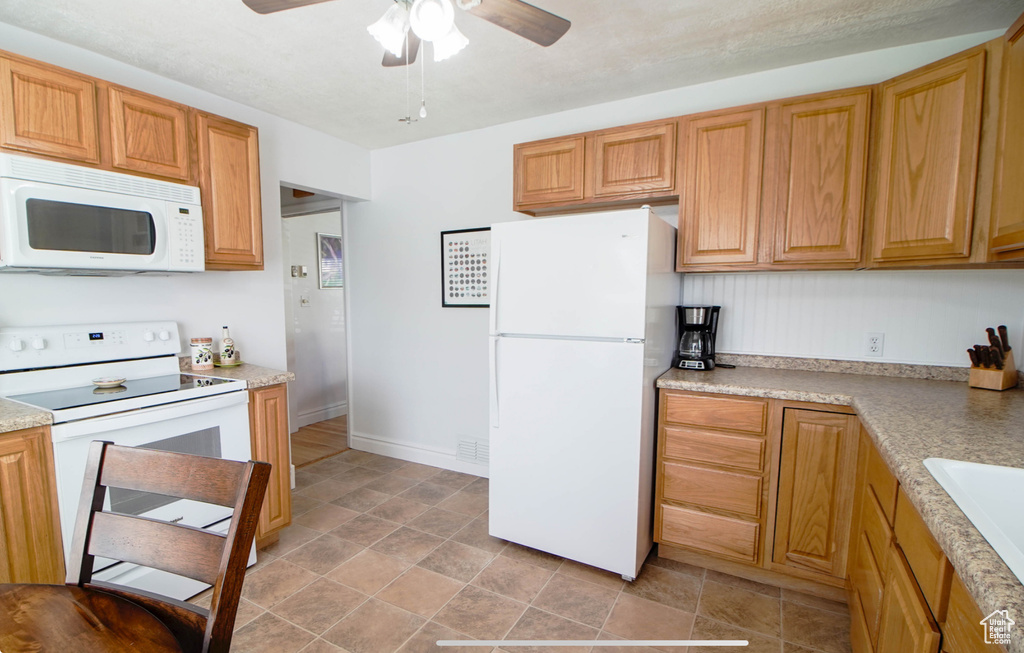 Kitchen with white appliances, ceiling fan, light countertops, stone finish floors, and a sink