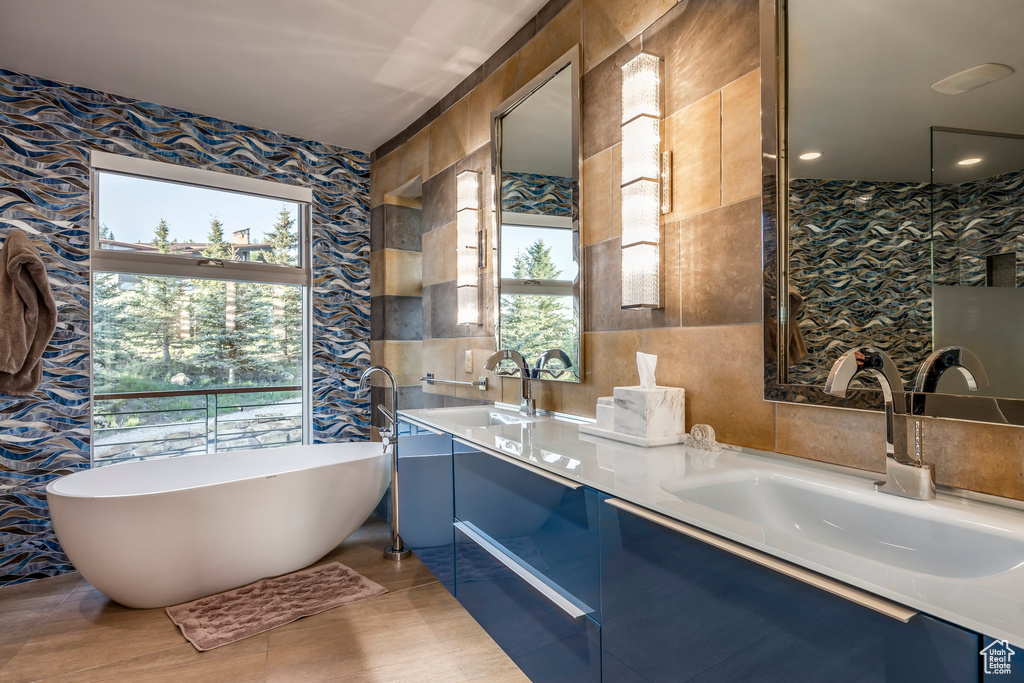 Bathroom with wallpapered walls, a freestanding tub, double vanity, and tile walls