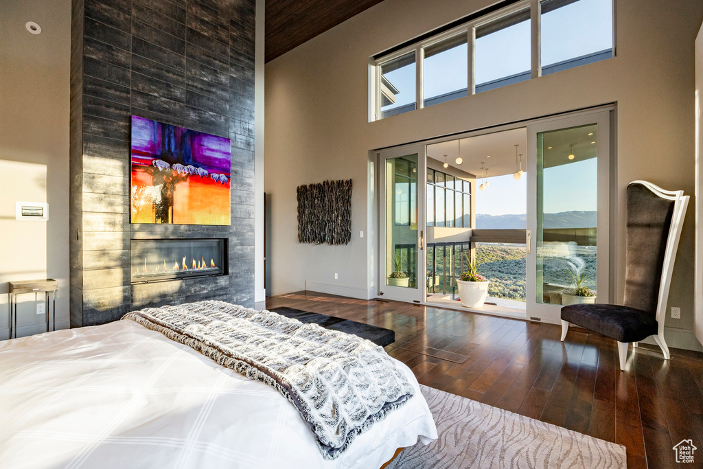 Bedroom with a towering ceiling, access to outside, wood-type flooring, a fireplace, and baseboards