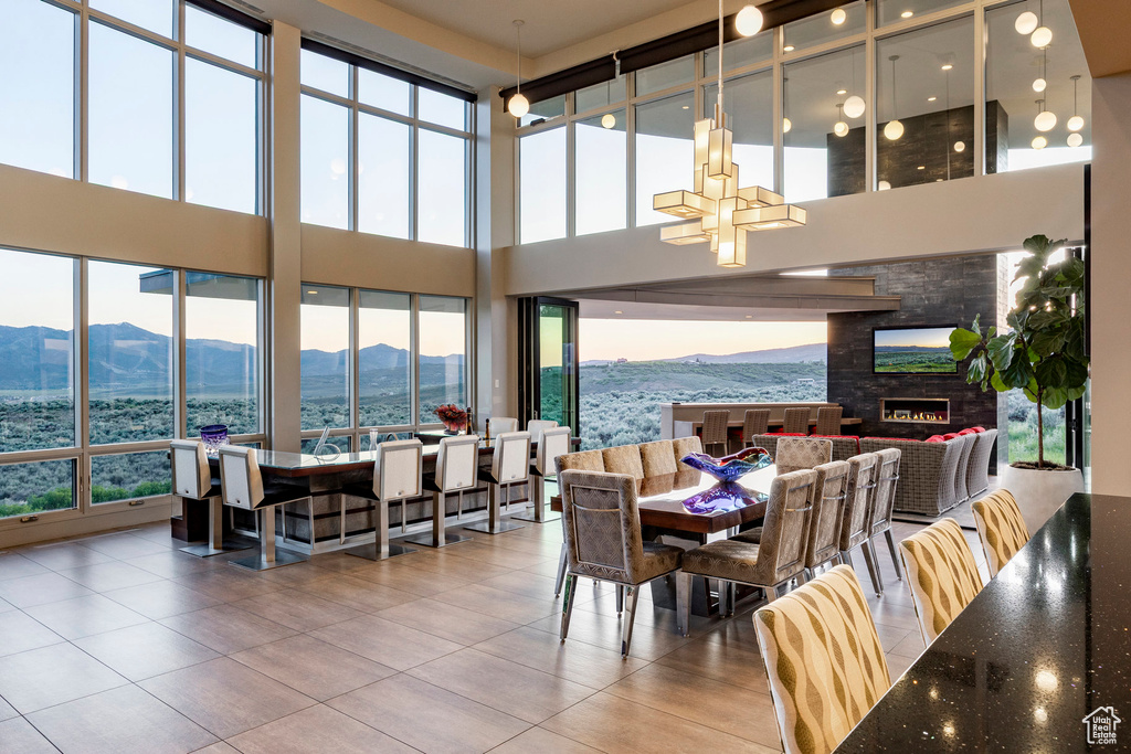 Tiled dining area with a chandelier, plenty of natural light, a high ceiling, and a stone fireplace