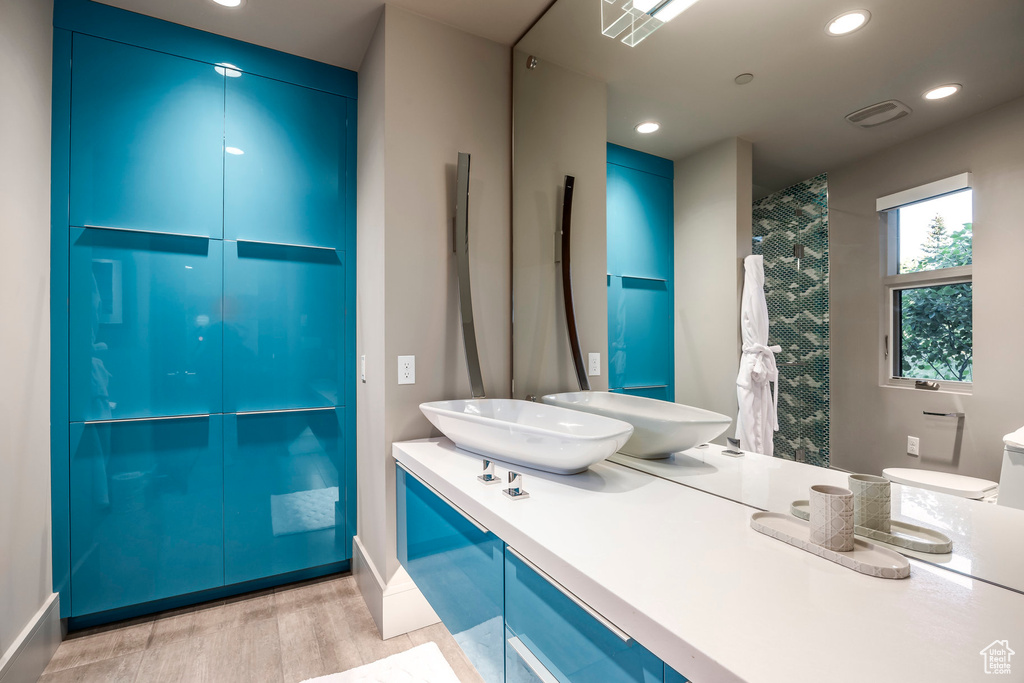 Full bathroom featuring wood finished floors, double vanity, baseboards, and recessed lighting
