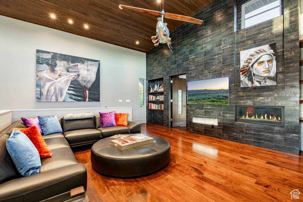 Living area with wood finished floors, a tiled fireplace, built in features, wood ceiling, and a towering ceiling