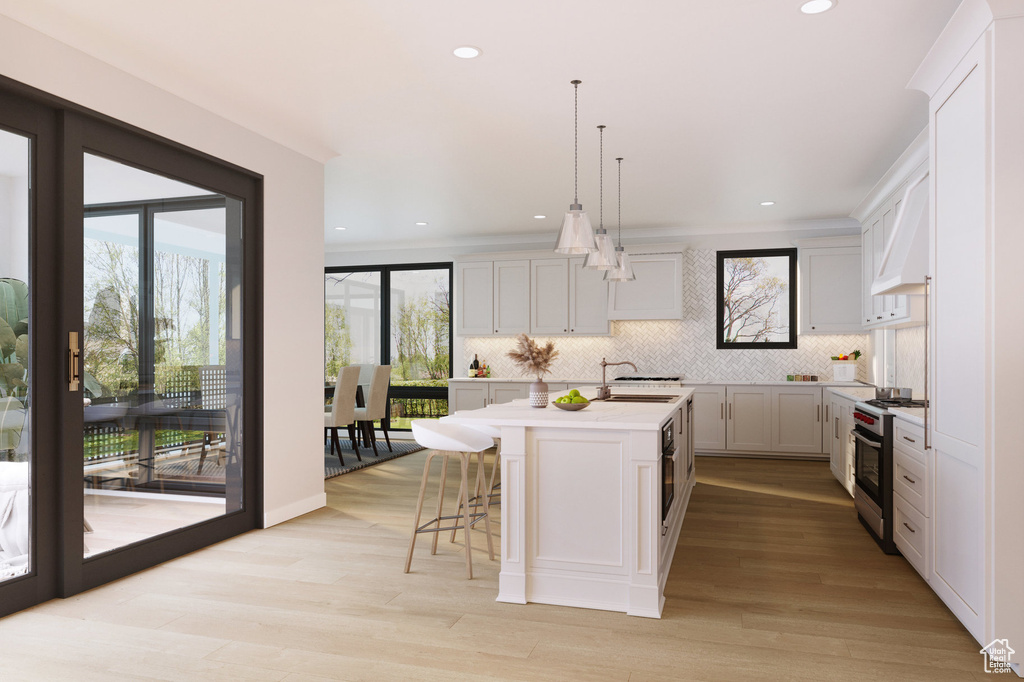 Kitchen featuring stainless steel range, light countertops, decorative backsplash, a center island with sink, and a sink