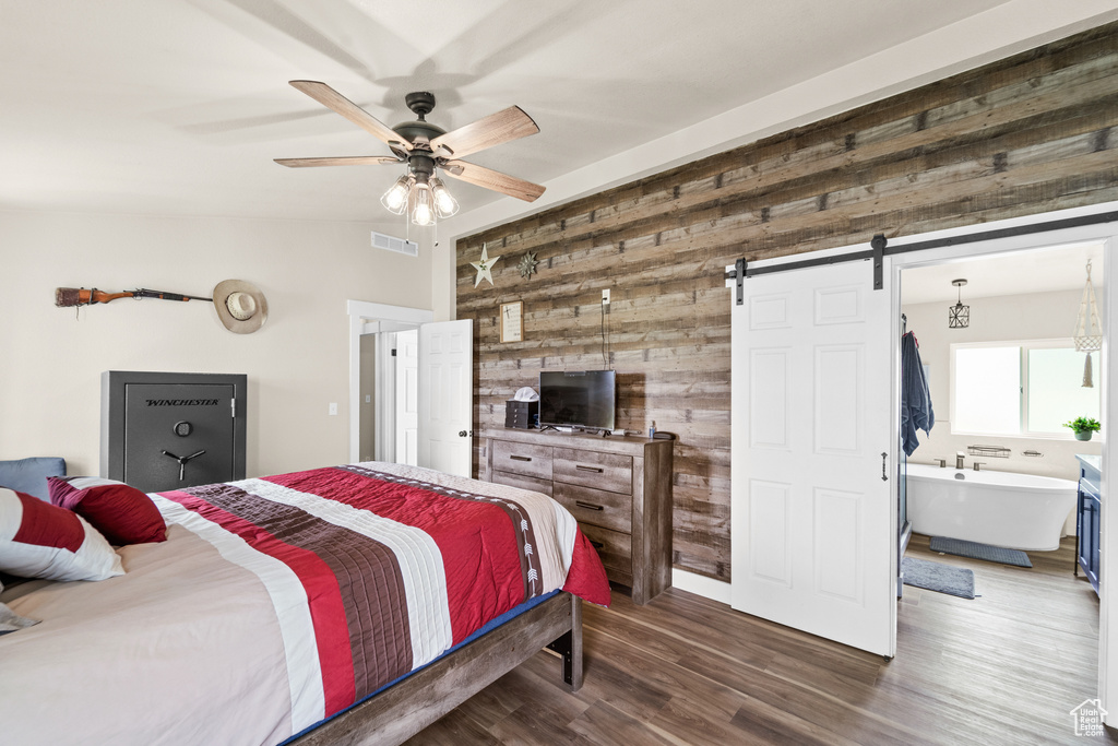 Bedroom with wood walls, a barn door, dark wood finished floors, vaulted ceiling, and a ceiling fan