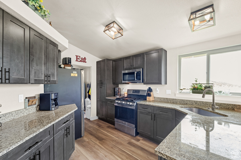 Kitchen featuring appliances with stainless steel finishes, a sink, light stone counters, light wood-style flooring, and vaulted ceiling