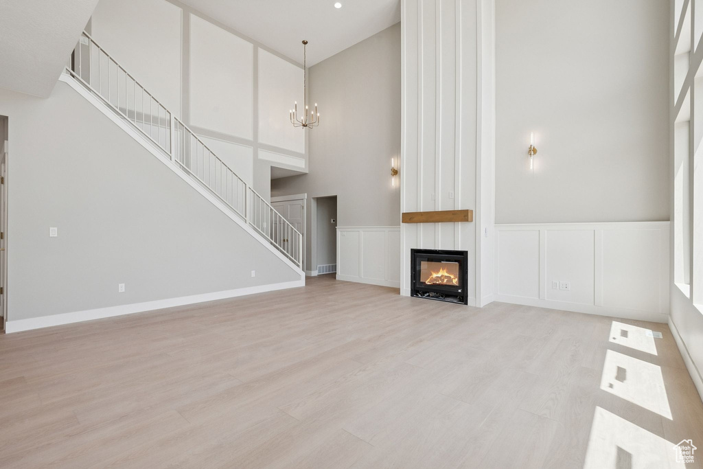 Unfurnished living room with a high ceiling, a chandelier, stairway, a large fireplace, and light wood-type flooring