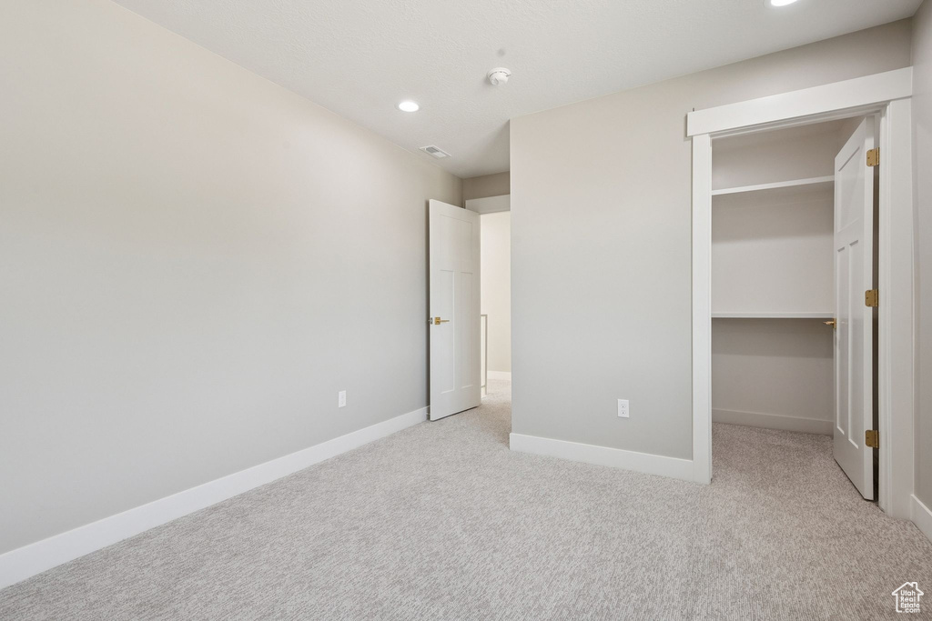 Unfurnished bedroom featuring light colored carpet, a walk in closet, baseboards, recessed lighting, and a closet