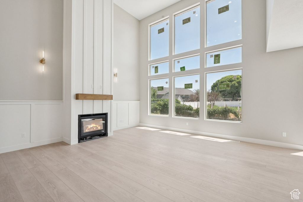 Unfurnished living room with plenty of natural light, wood finished floors, a fireplace, a high ceiling, and a wainscoted wall