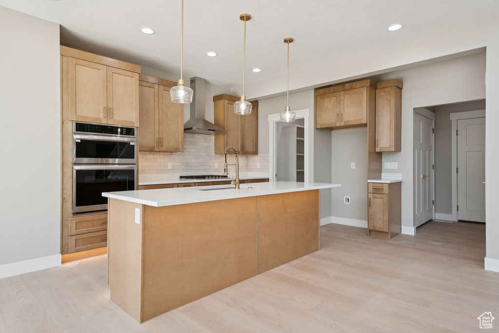 Kitchen featuring wall chimney range hood, a sink, stainless steel double oven, tasteful backsplash, and light wood finished floors