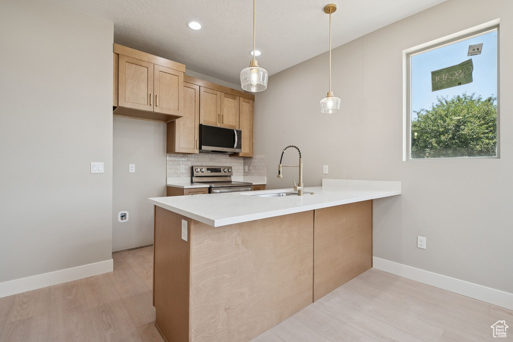 Kitchen featuring appliances with stainless steel finishes, a sink, a peninsula, tasteful backsplash, and light brown cabinets