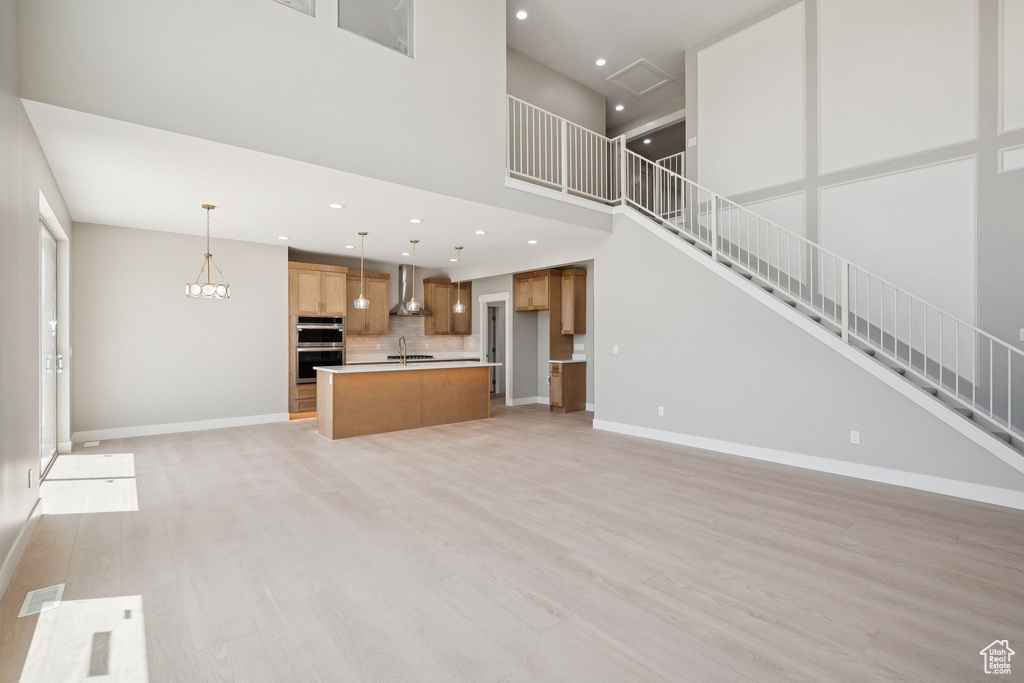 Unfurnished living room with a sink, a high ceiling, light wood-style floors, stairs, and baseboards