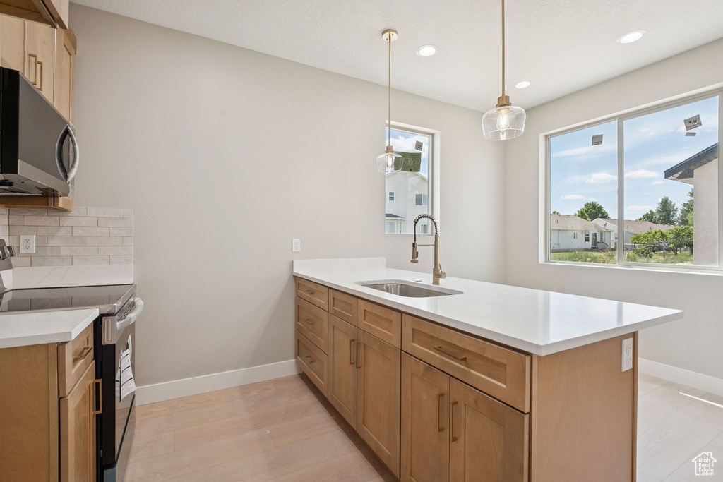 Kitchen with black range with electric cooktop, a sink, stainless steel microwave, a peninsula, and light countertops