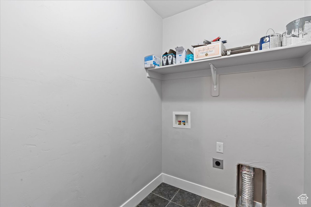 Laundry area with hookup for an electric dryer, hookup for a washing machine, dark tile patterned floors, and baseboards