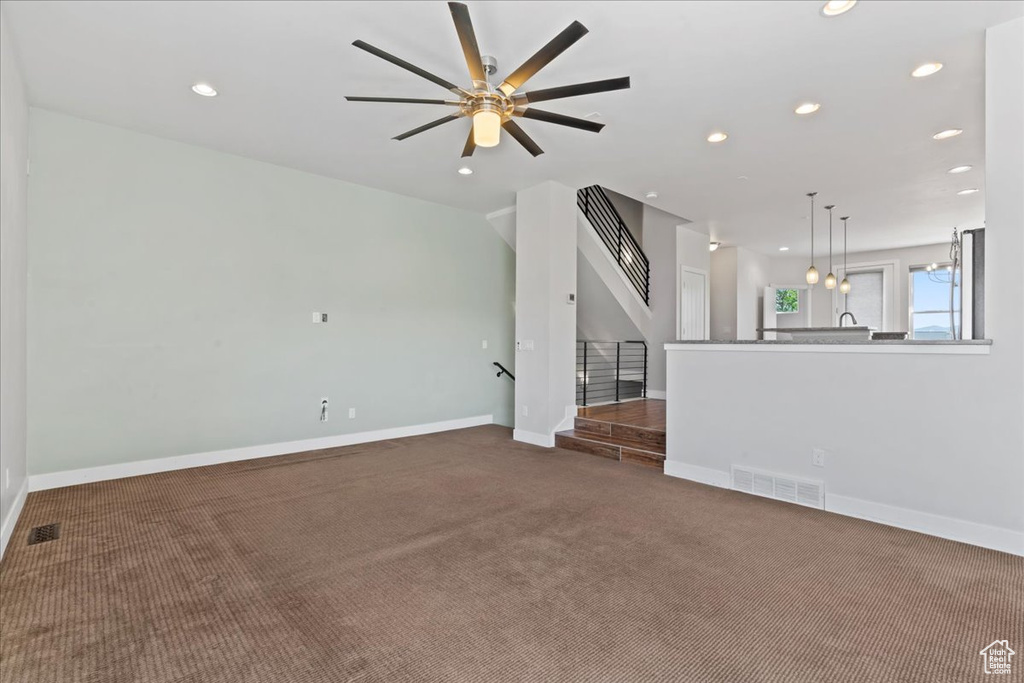 Unfurnished living room featuring carpet flooring, recessed lighting, baseboards, a ceiling fan, and stairs