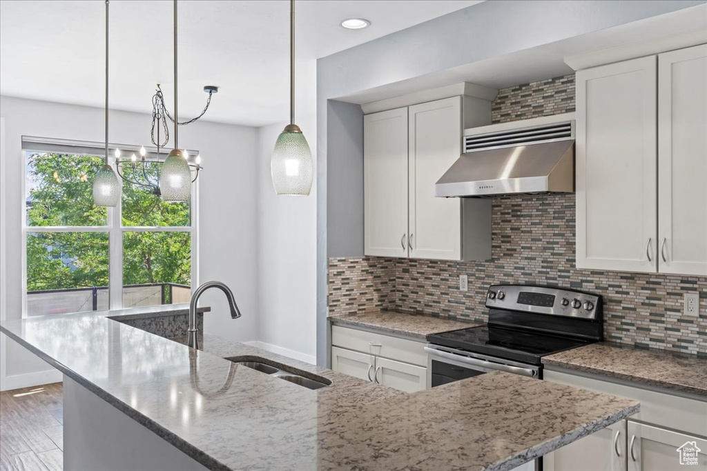 Kitchen with wall chimney exhaust hood, a sink, light stone countertops, and backsplash