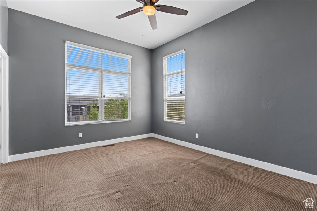 Carpeted empty room featuring ceiling fan and baseboards