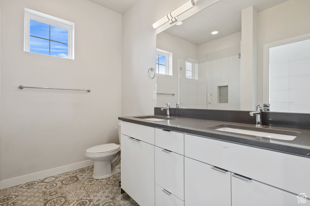 Bathroom featuring baseboards, double vanity, toilet, and a shower with shower door