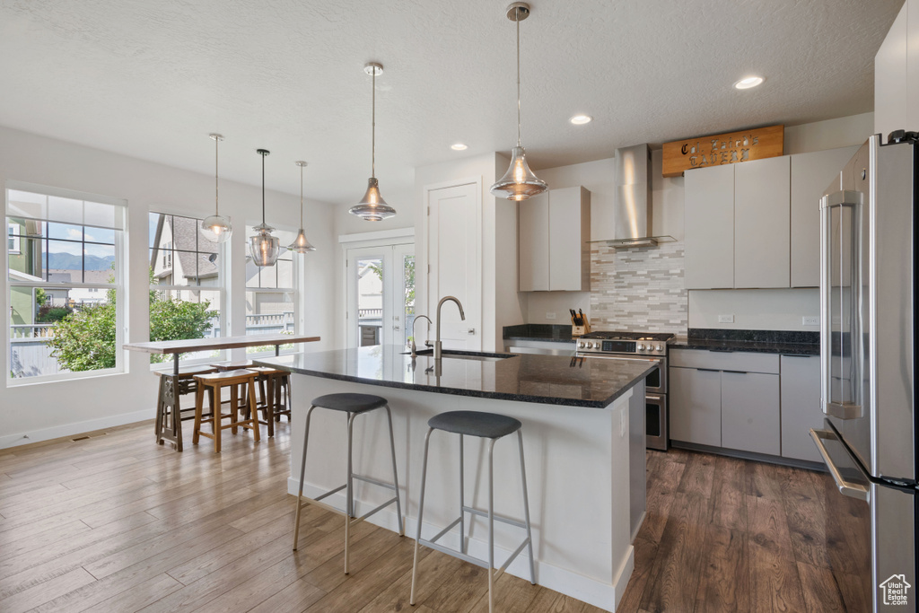 Kitchen featuring stainless steel appliances, wall chimney exhaust hood, a sink, a kitchen breakfast bar, and dark wood-type flooring