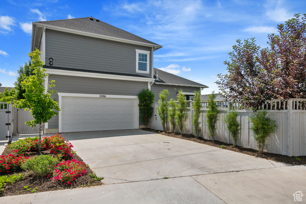 View of side of home with a garage, concrete driveway, and a shingled roof