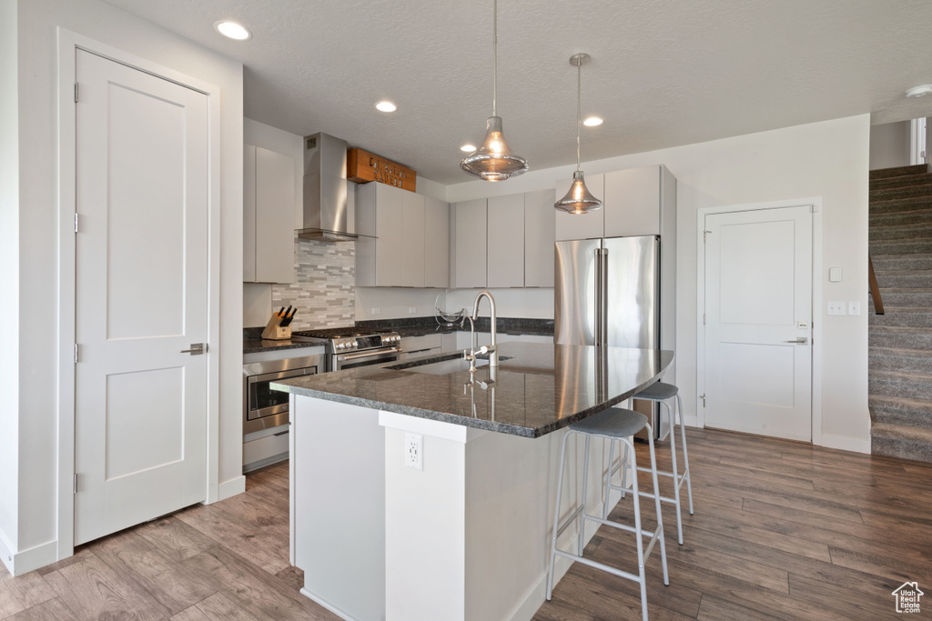 Kitchen featuring wall chimney range hood, a sink, appliances with stainless steel finishes, a kitchen breakfast bar, and wood finished floors