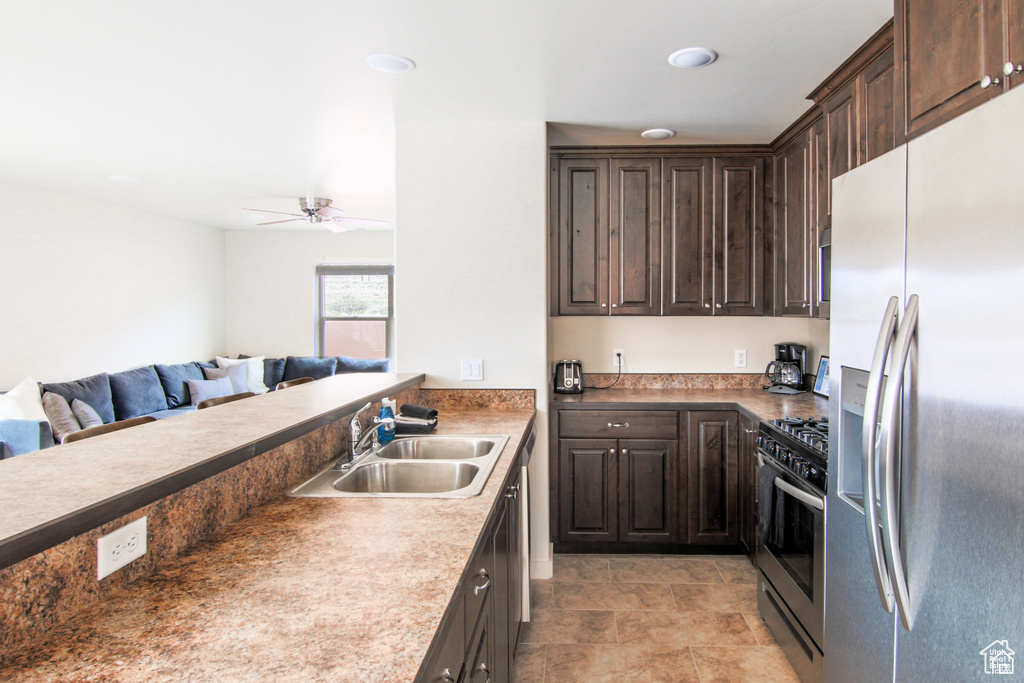 Kitchen featuring appliances with stainless steel finishes, a sink, open floor plan, dark brown cabinetry, and a ceiling fan