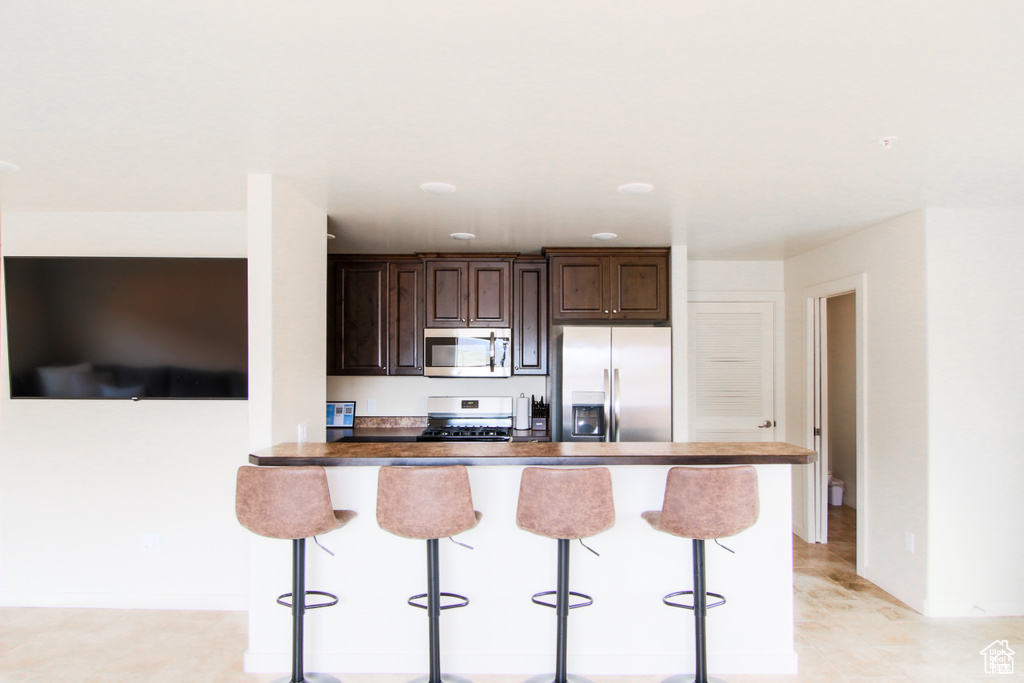 Kitchen featuring appliances with stainless steel finishes, a kitchen breakfast bar, dark brown cabinetry, and baseboards