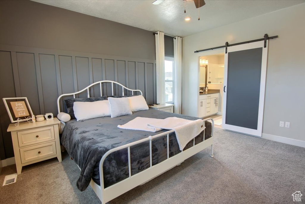 Bedroom with a barn door, light colored carpet, ensuite bathroom, and a ceiling fan