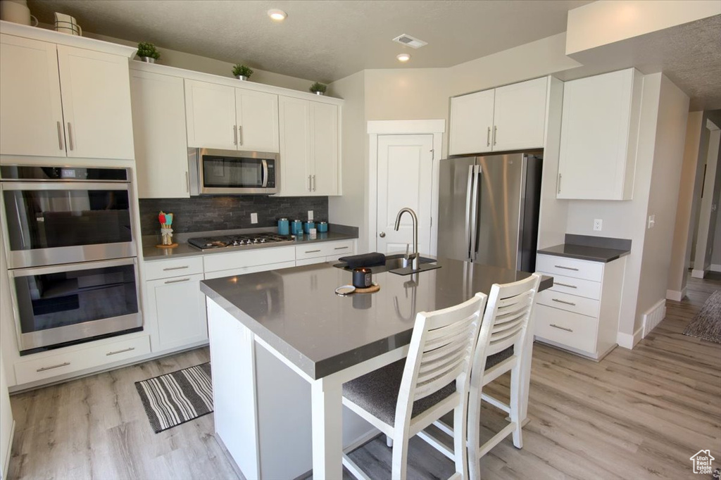 Kitchen with appliances with stainless steel finishes, a sink, light wood-style flooring, tasteful backsplash, and recessed lighting
